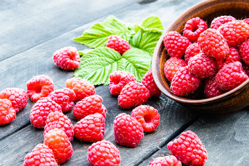 Ripe red raspberries on a bowl on the background of the old dark boards. Selective focus.