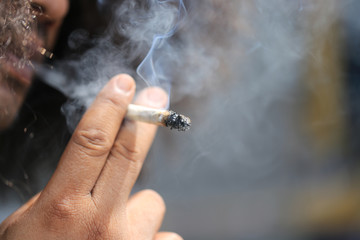 Bearded man smoking a marijuana cannabis joint or smokes a cigarette on green background, Medical marijuana should not be used in illegal ways, Stop smoking concept © Monthira