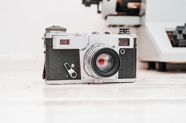 Old film camera on white plank background. Typewriter on the background. Vintage photo