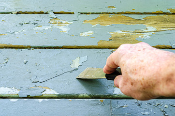 Man's hand shown scraping old paint on wood boards