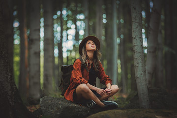 Style girl with backpack sitting in a stone in a summer time mixed coniferous forest