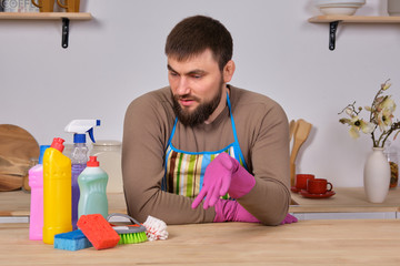 Young handsome bearded man in the kitchen, shows all his cleaning staff - detergents, brushes, sprays. He think he is ready for real cleaning