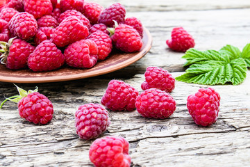 Ripe red raspberries on a bowl on the background of old boards. Selective focus.