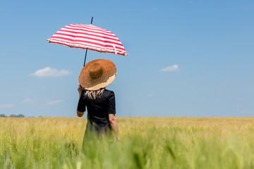 Female in black dress and hat with red umbrella stay in wheat field