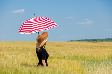 Female in black dress and hat with red umbrella stay in wheat field