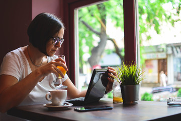 Young woman drinking coffee in cafe and using tablet computer, laptop, mobile.Modern business woman in city cafe.