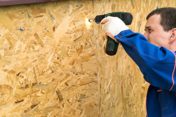 master in a blue uniform works as a screwdriver fastens wooden shields