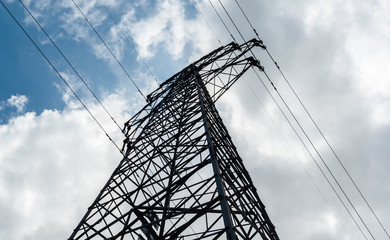 A high-voltage electricity pylon against blue sky with clouds at sunny day. High-voltage power transmission tower. Power engineering.