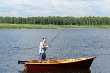 a man in a boat on a river rejoices when a fish is caught spinning while pulling it out of the water