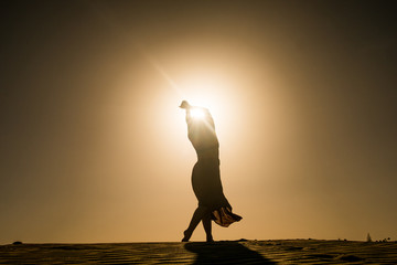 silhouette of young woman with long skirt dancing in evocative and confident way on top of desert...