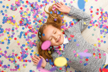 Top view of a little girl lying on the floor under falling confetti.