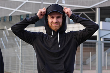 Charismatic man with red beard in a black cap and black hoodie. Street brand advertising. Fashion and style. Mockup.