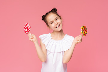 Adorable little girl enjoying sugar treat, holding two big colorful lollipops