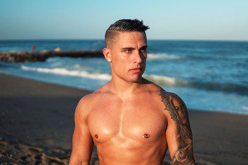 Tattooed bodybuilder sexy male coach at the beach. He stands and shows his muscles