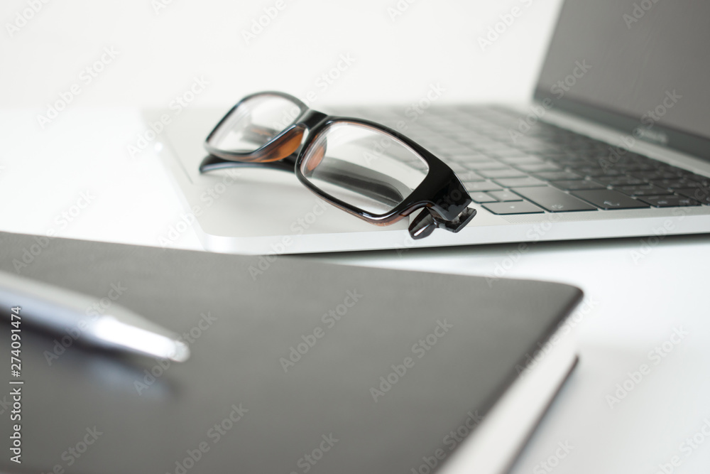 Poster close-up of eye glasses on a computer on a modern table in white with pen and notebook.