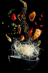 flying wok with chicken and spices. Concept of food preparation in low gravity mode, food levitation. Separated on black background. High resolution image - obrazy, fototapety, plakaty