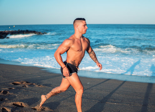 Tattooed bodybuilder sexy male coach at the beach. He runs and shows mucles