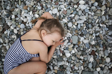 tired child on beach, girl in swimsuit is resting