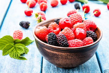 Fruits and berries in a bowl on a blue wooden background. Ripe raspberry, cherry, mulberry.