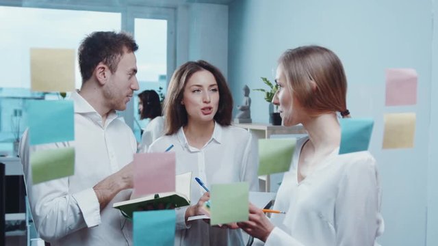 Group of cheerful workers planning and brainstorm writing over the project with stickers note on glass window at modern office.Teamwork, management and cooperation concept. Close up view