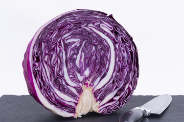 Fototapeta premium A purple cabbage cut in half accompanied by a knife on a black cutting board