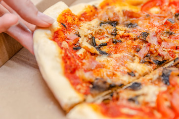 Female hand takes a piece of pizza from the box on the kitchen table close up
