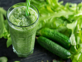 Green cucumber smoothie for weight loss in a glass on a wooden dark table with ingredients
