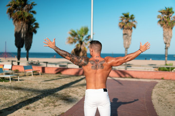 Obraz premium Tattooed bodybuilder sexy male coach at the beach. He poses for the camera and shows his muscles