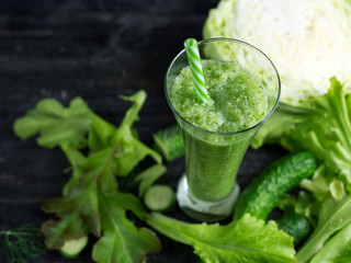 Green cucumber smoothie for weight loss in a glass on a wooden dark table with ingredients