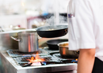 Chef cooking with flame in a frying pan on a kitchen stove.
