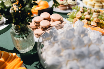 Details of a festival catering: fruits, cupcakes, macaroons and burgers. Sweet table at the feast. Delicious candy bar at the wedding ceremony close up. Catering service plate. Wedding party concept