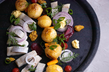 New potatoes on a black dish, a number of pieces of herring, red onion, chips of beet, sprigs of dill. 