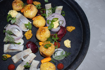 New potatoes on a black dish, a number of pieces of herring, red onion, chips of beet, sprigs of...