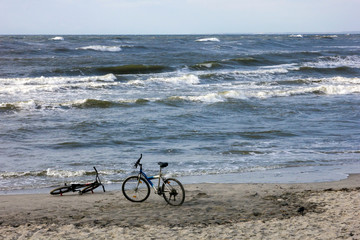 Two bicycles on a sandy beach against the waves of the Baltic sea.