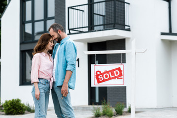 happy man and woman with closed eyes standing near house