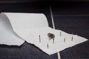 Silver big thumbtacks or drawing-pins on toilet paper.Hemorrhoids or urine problem concept. White...