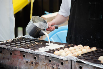 Street food chef Pouring ingredients on a special pan to make Takoyaki Japanese traditional food.