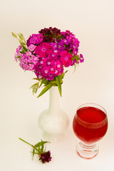  Transparent glass of fruit wine and a bouquet of Turkish carnations in a white vase