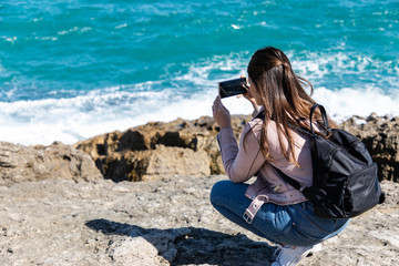 Woman crouching taking pictures of shore with smart phone