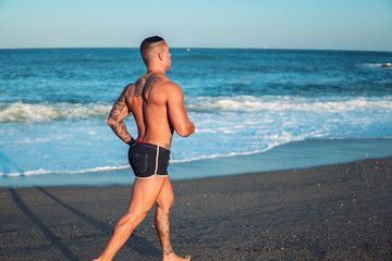 Tattooed bodybuilder sexy male coach at the beach. He runs and shows mucles