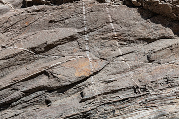 Superfície da rocha natural, com linhas de cristais brancos. Textura da superfície da rocha natural, onde se podem ver as camadas de rocha e linhas de cristais brancos formados ao longo do tempo.