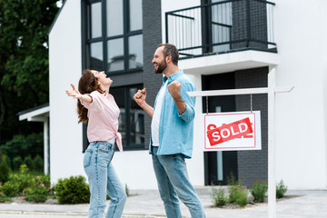 happy man and woman celebrating near house and board with sold letters