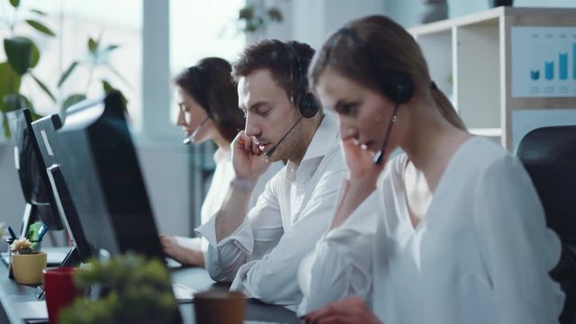 Close up view of line of professional customer support, male and woman synchronically answer the calls via the headset. Working hard, teamwork, cooperation. Business management success concept