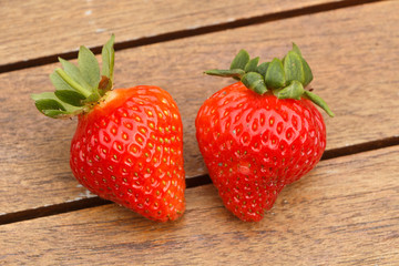 Two strawberries with their leaves on a wooden table