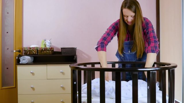 A young pregnant woman in preparation for a newborn child is prepared for the meeting. Folding children's wooden furniture, cradles, crib. Build furniture - baby cot. Medium shot.