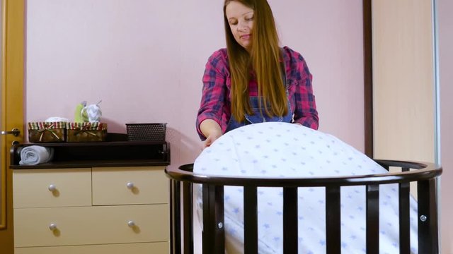 A young pregnant woman in preparation for a newborn child is prepared for the meeting. Folding children's wooden furniture, cradles, crib. Build furniture - baby cot. Medium shot.