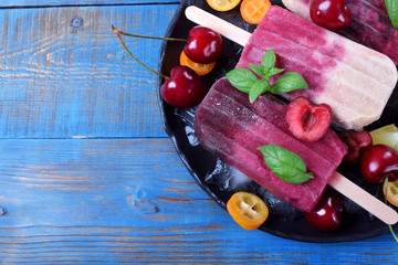 Fruit and berry popsicles on the plate with ice, pieces of kumquat, lime and cherries and mint...