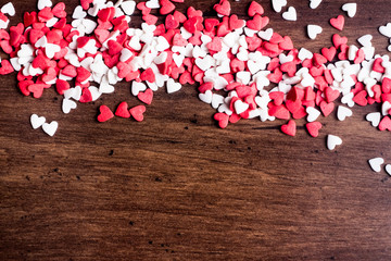 Valentines Day background with red and white hearts on a wooden table, top view. Red heart shaped candies on a wooden brown background. The concept of Valentines Day. 
