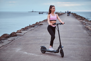 Beautiful young woman is posing for photographer at seaside with her electrical scooter.