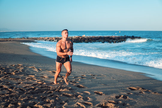 Tattooed bodybuilder sexy male coach at the beach. He runs and shows mucles